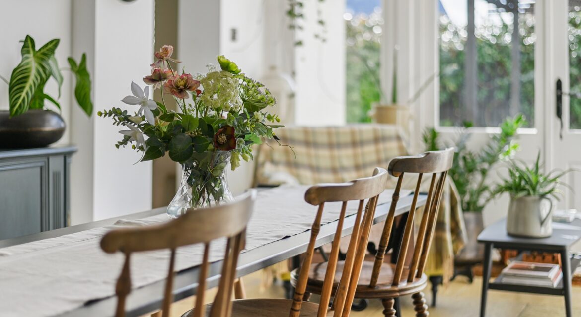 Bright dining room with wooden chairs, long table and fresh flower arrangement by patio doors