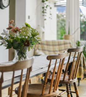 Bright dining room with wooden chairs, long table and fresh flower arrangement by patio doors