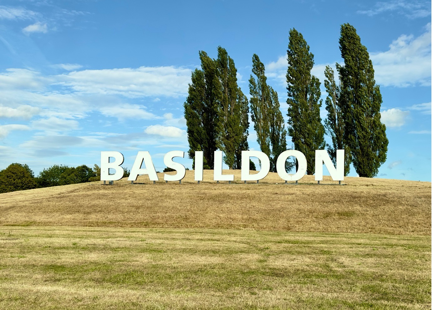 Large Basildon sign on grassy hill with trees and blue sky background